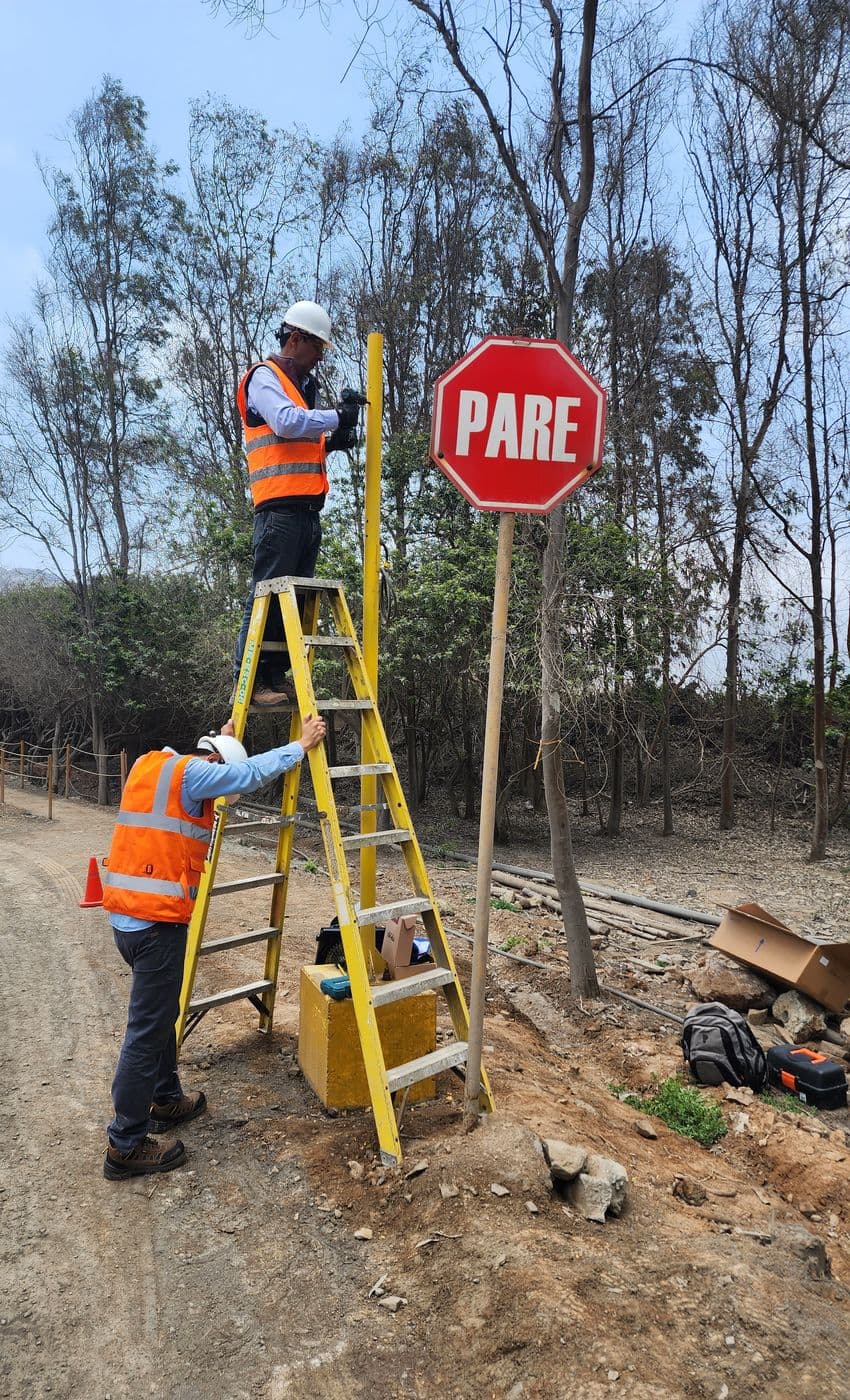 Dos técnicos montan sobre una escalera el poste de un semáforo de seguridad vial junto a una señal de PARE.