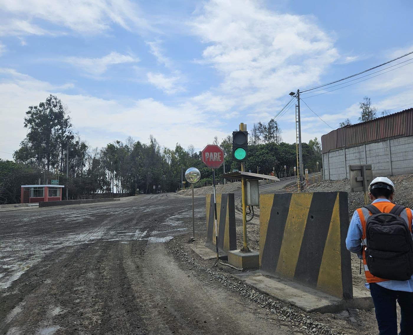 Semáforo de seguridad en verde en el acceso a una operación minera, con un técnico caminando hacia el cruce.